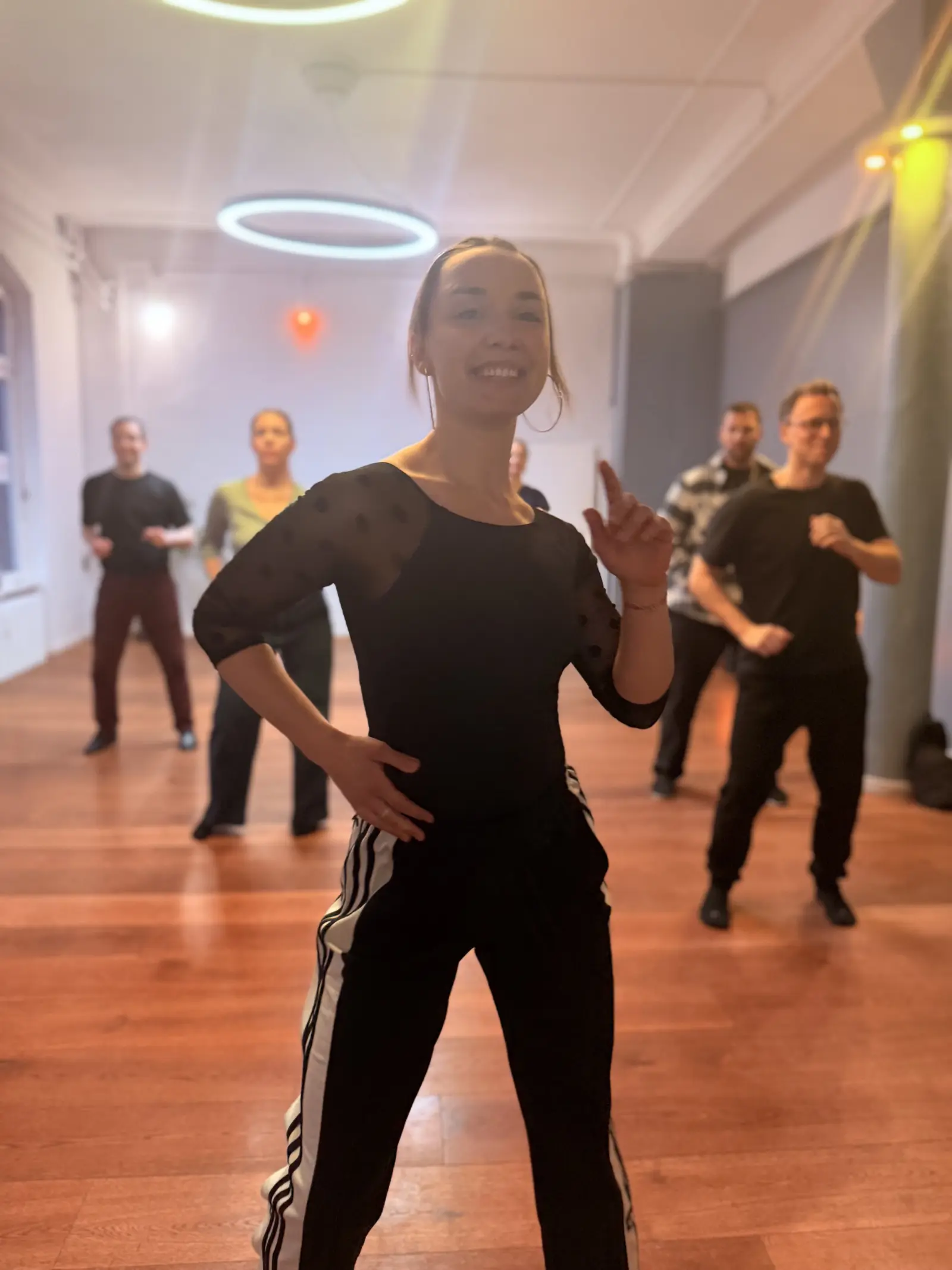 Lucy smiling while teaching a salsa class with students in soft focus behind